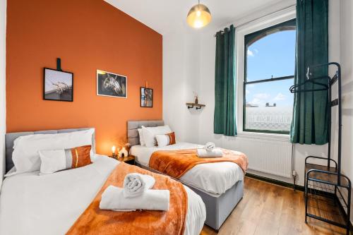 two beds in a room with orange walls and a window at Spacious Birmingham City Apartment in Birmingham