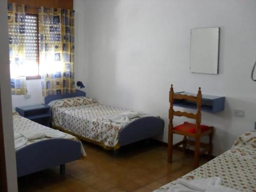 Habitación con 3 camas, silla y mesa. en Hotel Pourally, en Villa Gesell