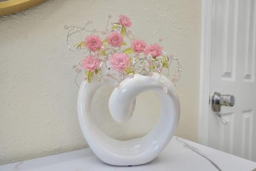 a white vase with pink flowers in it at Family Fun Oasis Pool Hot Tub and Play Area in Houston
