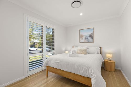 a white bedroom with a bed and a window at Pipis Huskisson by Experience Jervis Bay in Huskisson
