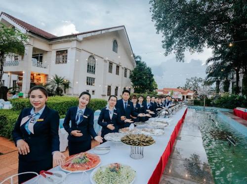 a group of people standing at a long table with food at Dakruco Hotel in Buon Ma Thuot