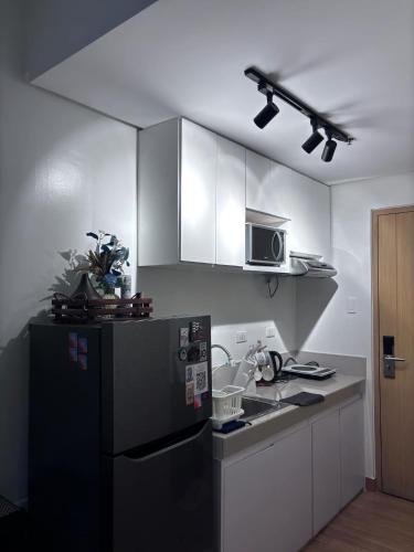 a kitchen with a black refrigerator and white cabinets at Cozy Near Mall SM Fairview Trees Residences Quezon City in Manila