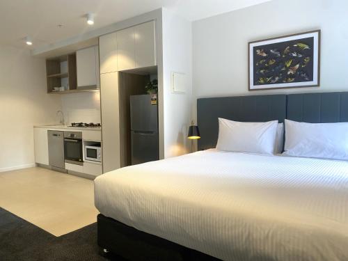 a bedroom with a large white bed and a kitchen at Brady Apartment Hotel Hardware Lane in Melbourne