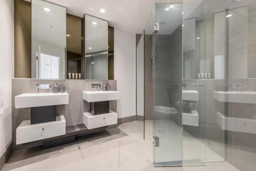 ein Badezimmer mit zwei Waschbecken und einer Glasdusche in der Unterkunft West Side Spencer St Apt w Marvel Stadium View in Melbourne
