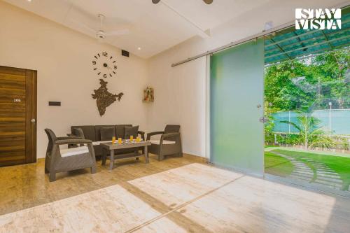 a living room with chairs and a table and a clock at Sundream Palms by VEO - Part of StayVista with Pool, Lawn, BBQ in Alibag