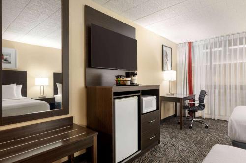 a hotel room with a bed and a desk with a television at Ramada by Wyndham Alpena in Alpena