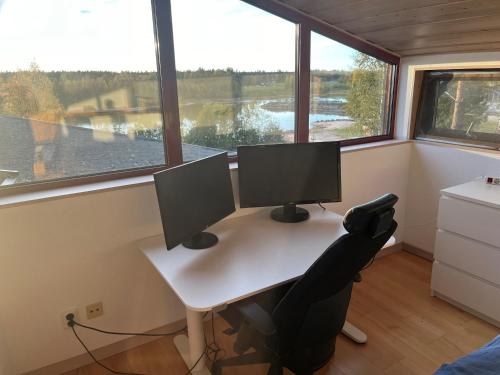 a computer desk with two monitors on it in a room with windows at The paradise by the beach in Långviken