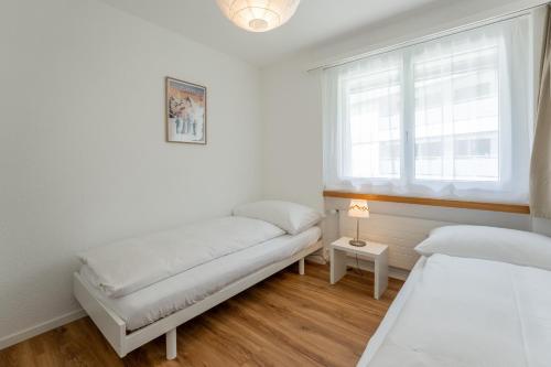 deux lits dans une chambre blanche avec une fenêtre dans l'établissement LAAX Homes - Haus Ner B 29, à Flims