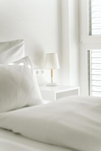 a white bedroom with a bed and a lamp at Sedan Apartments Günzburg - Nahe Legoland - Familienurlaub in Günzburg
