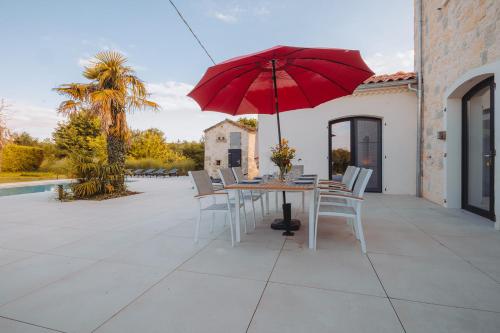 a table with a red umbrella on a patio at Villa au Petit Bonheur avec clim - Hameau au calme - piscine chauffée - pétanque in Moncrabeau