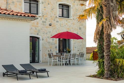 a patio with a table and chairs and a red umbrella at Villa au Petit Bonheur avec clim - Hameau au calme - piscine chauffée - pétanque in Moncrabeau