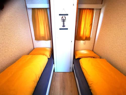 twee bedden in een kleine kamer met oranje gordijnen bij Bed and Breakfast Op het Broek in Harfsen