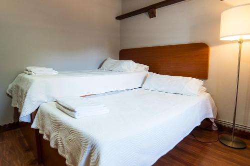 two beds in a room with white sheets and a lamp at Paratene Ostatu Habitaciones in Erandio