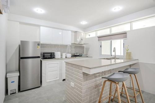 a white kitchen with a stainless steel refrigerator and stools at Haus Ekkamai 2 in Khlong Toei