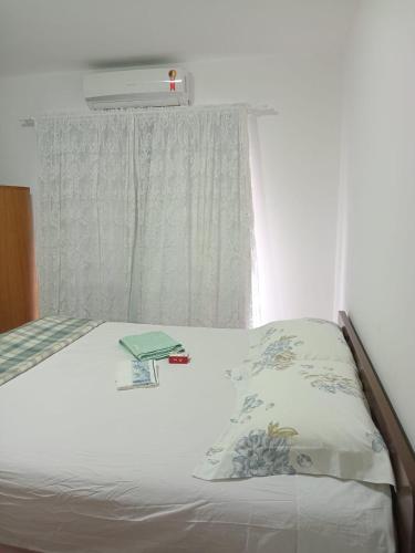a bed with a window with a pillow and a book at Suíte perto da Vila Germânica, em Blumenau in Blumenau