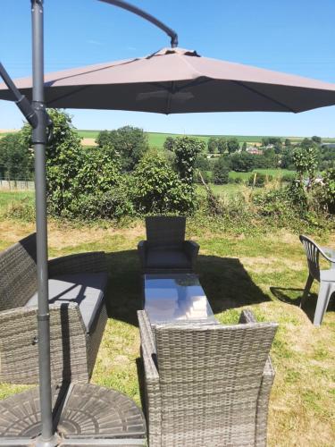a table and chairs under an umbrella in the grass at Au petit coin tranquille in Saint-Gobert