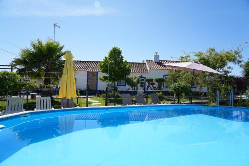 a large blue swimming pool with chairs and an umbrella at A Janela das Palmeiras in Reguengos de Monsaraz