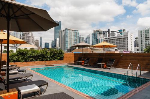 a swimming pool with chairs and umbrellas and a city skyline at The Dawin Hotel in Bangkok
