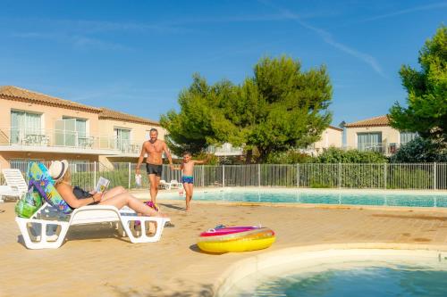 a woman sitting in a chair next to a swimming pool at Résidence Goélia Les Jardins De Phoebus in Gruissan
