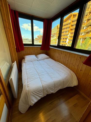 a bed in a room with three windows at Appartement Eskival skis aux pieds in Val Thorens