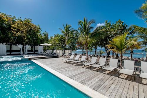 ein Pool mit Stühlen und Palmen und das Meer in der Unterkunft Emotions by Hodelpa - Juan Dolio in Juan Dolio
