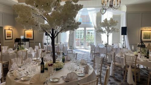 a dining room with white tables and chairs and a tree at Holiday Inn Milton Keynes East M1 Junc 14 by IHG in Milton Keynes