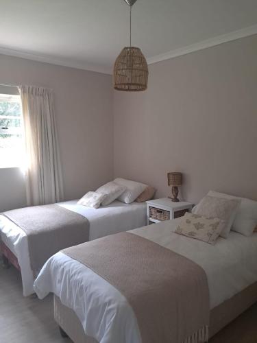 two beds in a white bedroom with a window at Sea Cottage in Noordhoek