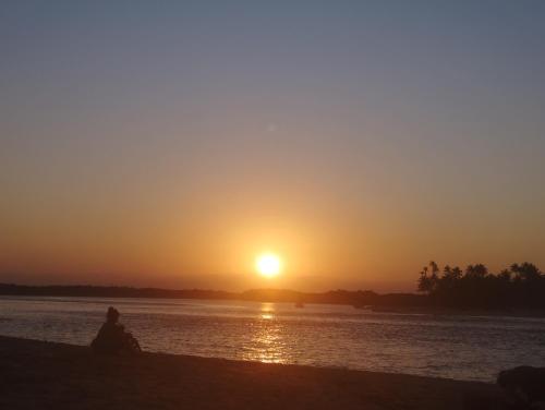 a person sitting on the beach watching the sunset at Pousada Horizonte in Ilha de Boipeba