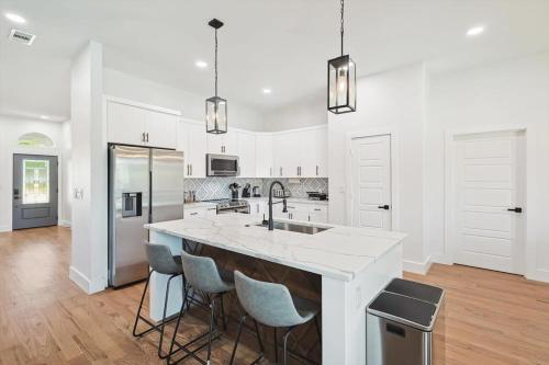 a white kitchen with a large island with bar stools at Paradise Modern Home Pool & Hot Tub for over 30 Nights in Waxahachie