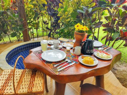 a wooden table with plates of food on it at BANGATACHO - Bangalôs Temáticos com Experiências Românticas Exclusivas - Praia do Patacho in Pôrto de Pedras