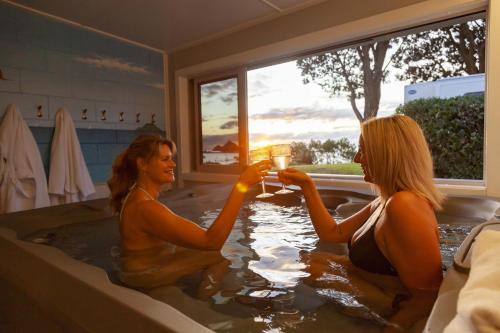 two women sitting in a bath tub with glasses of wine at Belt Road Seaside Holiday Park in New Plymouth