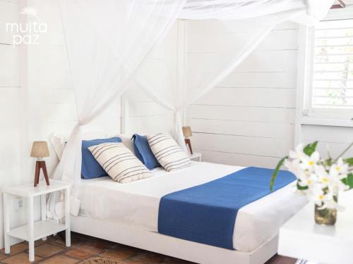 a white bedroom with a white canopy bed with blue and white pillows at Muita Paz in Atins