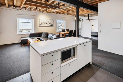 a living room with a white kitchen with a couch at Gibson Mill waterfront warehouse apartment - 201 in Hobart
