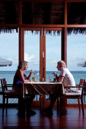 a man and woman sitting at a table with wine glasses at Adaaran Prestige Water Villas - with Dine around Premium All inclusive - 24 hours in Raa Atoll