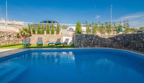a swimming pool with two chairs and a stone wall at Villa DIVINA with heated pool in Krk