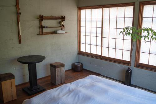 a bedroom with a bed and a table and windows at Machiya Guest House Carta in Kanazawa