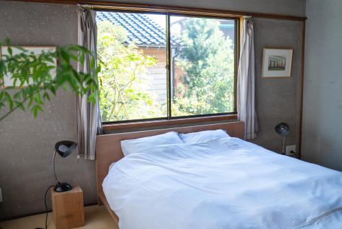 a bedroom with a white bed and a window at Machiya Guest House Carta in Kanazawa