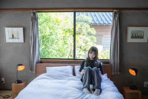 a girl sitting on a bed in front of a window at Machiya Guest House Carta in Kanazawa