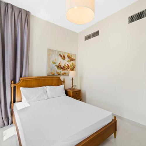 a bedroom with a white bed with a wooden frame at Modern 3-Bedroom Villa in Damac Hills 2 in ‘Ūd al Bayḑāʼ