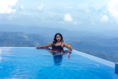 a woman in a infinity pool with a glass of wine at Le Montfort Resort in Munnar