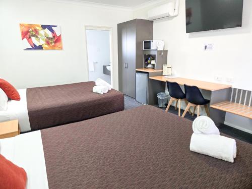 a hotel room with two beds and a desk with chairs at Ascot Lodge Motor Inn in Kingaroy