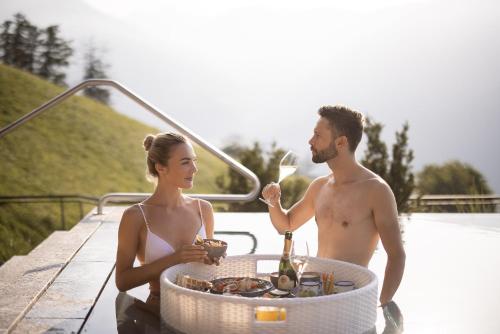a man and a woman standing on a dock with a table with wine glasses at DAS GERSTL Alpine Retreat in Malles Venosta