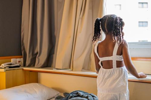 a young girl looking out of a window at ibis Santo Andre in Santo André