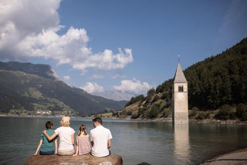 a group of people sitting on a rock in a lake with a tower at DAS GERSTL Family Retreat in Resia