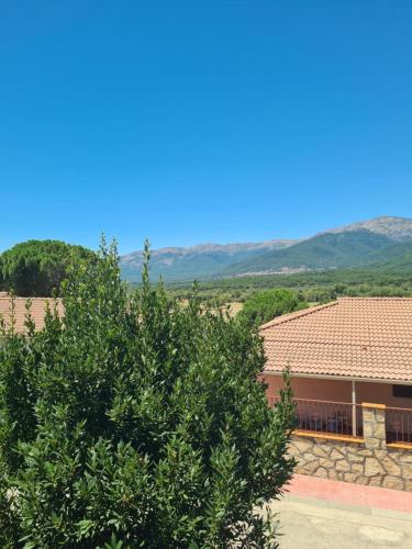 a tree in front of a house with mountains in the background at El Castillo in La Adrada
