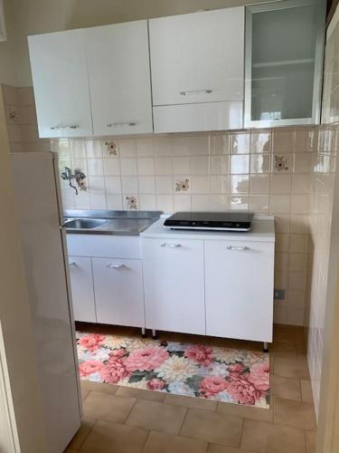 a kitchen with white cabinets and pink flowers on the floor at La casa di Giulio e Lina in Fossombrone