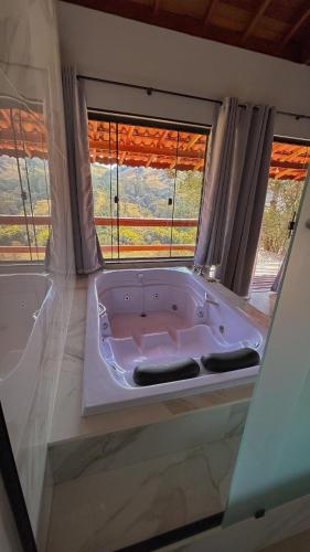 a bath tub in a bathroom with two windows at Chalés Recanto na Serra in Gonçalves