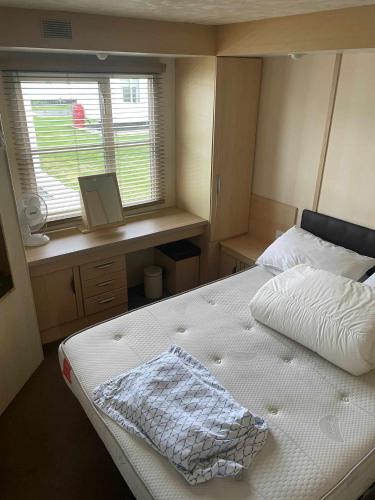 a bedroom with a bed and a desk and a window at PG101 6 BERTH DELUXE ON THE GOLDEN PALM CHAPEL st LEONARD PG101 in Chapel Saint Leonards