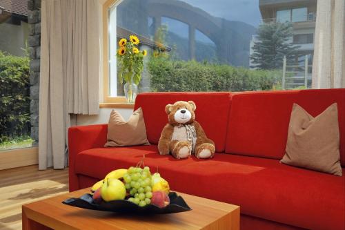 a teddy bear sitting on a red couch with fruit on a table at Ferienwohnungen Waldruhe in Santa Valburga St. Walburg