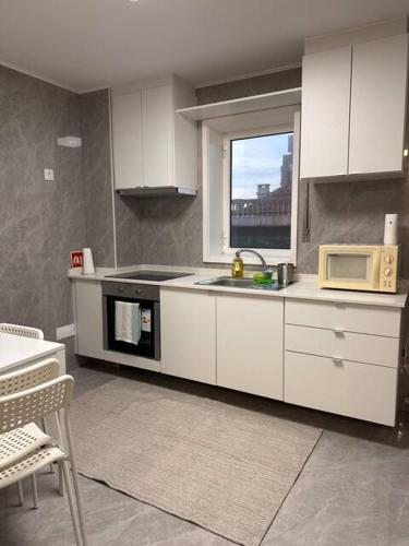 a kitchen with white cabinets and a microwave and a window at Confortável ensuite 1 privado centro da cidade in Póvoa de Varzim